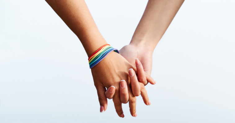 two women's clasped hands with rainbow bracelet