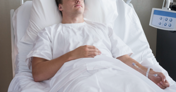 A man lying down in a hospital bed attached to an IV.