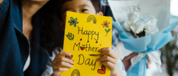 A child holding a mother's day card sitting on a woman's lap.