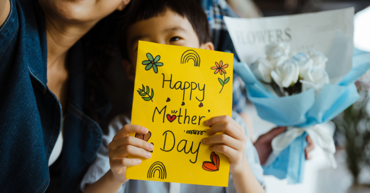 A child holding a mother's day card sitting on a woman's lap.