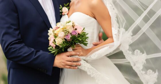 Bride in beautiful white wedding dress with bouquet and elegant groom in blue suit at happy wedding day.