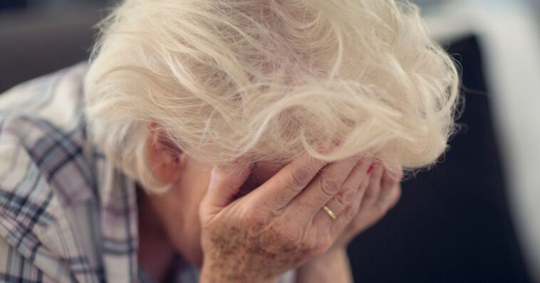 Senior woman holding her head in her hands in despair.