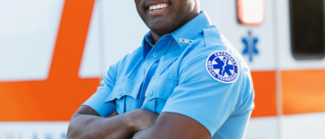 A male paramedic in uniform standing in front of an ambulance.