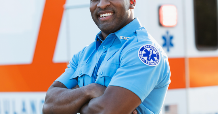 A male paramedic in uniform standing in front of an ambulance.