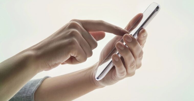 Young woman's hands using a portable information device on white background.