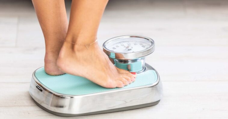 Woman standing on scale, close-up of legs and feet.