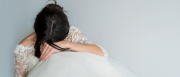 A woman wearing a wedding gown seated with her head in her hands.
