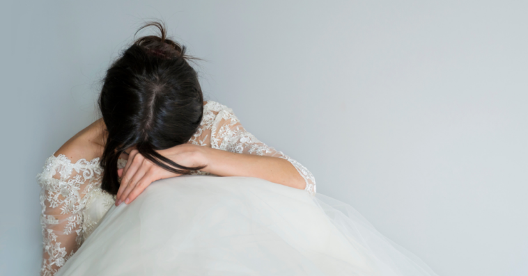 A woman wearing a wedding gown seated with her head in her hands.