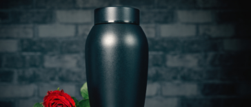 An urn with a rose lying next to it.