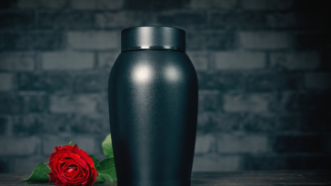 An urn with a rose lying next to it.