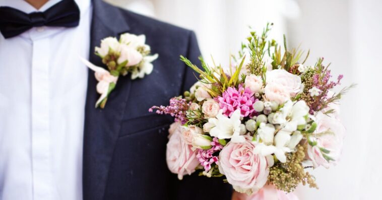 Close-up of a man in a tux holding a wedding bouquet.
