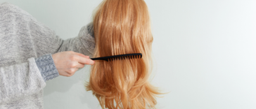 A woman holding a wig and running her comb through it.
