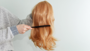 A woman holding a wig and running her comb through it.