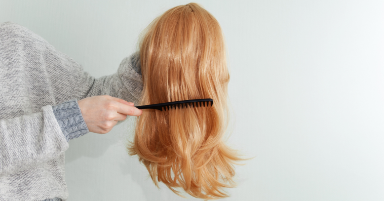 A woman holding a wig and running her comb through it.