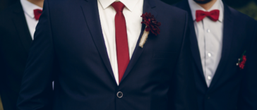 three men in matching blue suits with red boutonnieres and ties