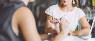 Two women sitting across from one another at a table having a tense conversation.