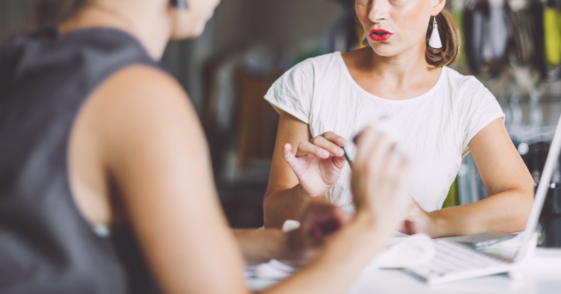 Two women sitting across from one another at a table having a tense conversation.
