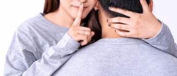 woman and man embrace as woman puts finger to lips to shush someone