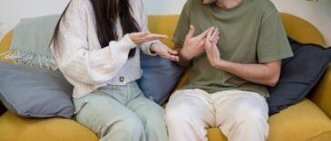 Young boyfriend and girlfriend sitting on sofa near potted plant and quarreling while having problems in relationship.