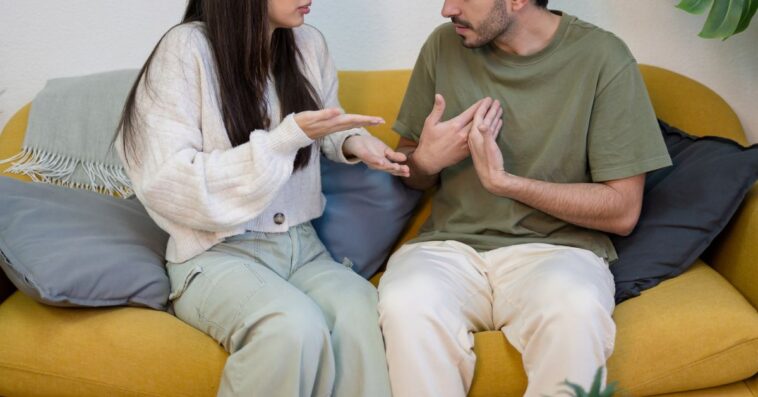 Young boyfriend and girlfriend sitting on sofa near potted plant and quarreling while having problems in relationship.