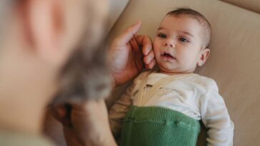 Portrait of cute calm baby lying on sofa, father caressing his soft cheek