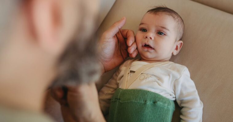 Portrait of cute calm baby lying on sofa, father caressing his soft cheek
