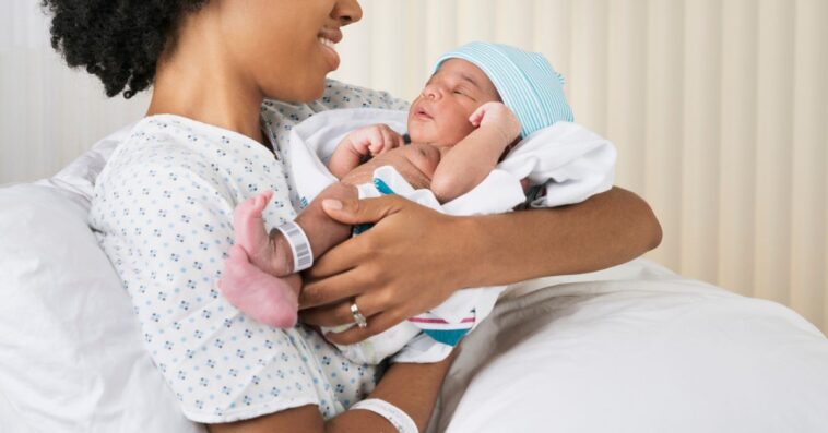Smiling mother holding newborn baby in hospital.