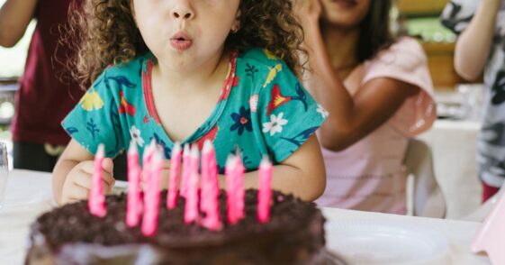 A small group of people, family, children, food, birthday cake, blowing out the candles.