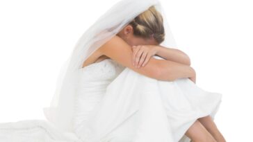 Unhappy blonde bride sitting on floor hiding her face.