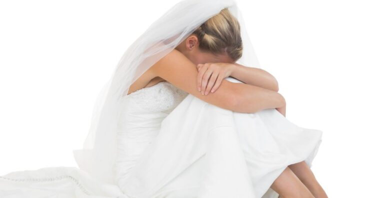Unhappy blonde bride sitting on floor hiding her face.