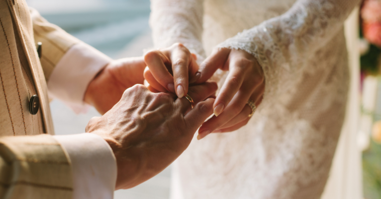 A bride slipping a ring on her groom's finger.