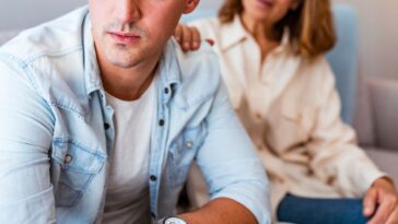 Mature Mother and problem child. Frustrated mother talking to with her upset son sitting on the couch. Senior mother talking with her unhappy son at home during the day. Mother comforting her black hair sad son.