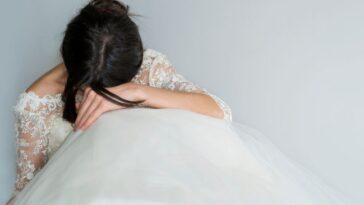 Beautiful Tired and Sad Bride sits on the floor with her head in her lap.