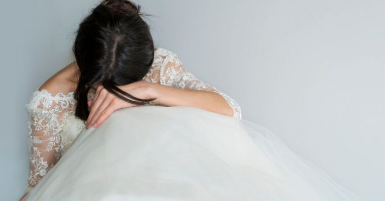 Beautiful Tired and Sad Bride sits on the floor with her head in her lap.