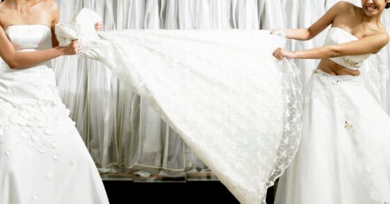 Young women in fitting room tugging at gown.