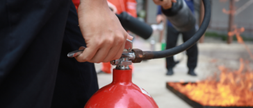 A hand holding a fire extinguisher with a fire in the background.