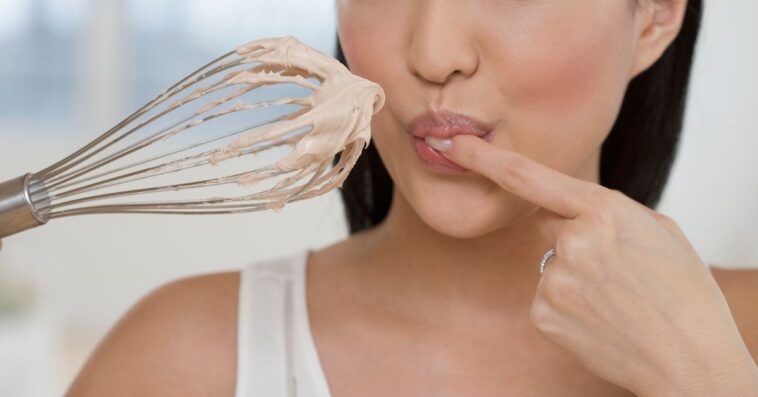 Close up of a woman tasting batter on a whisk.