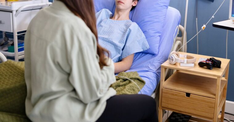 Portrait of a male teenager talking with his friend while lying in the hospital.
