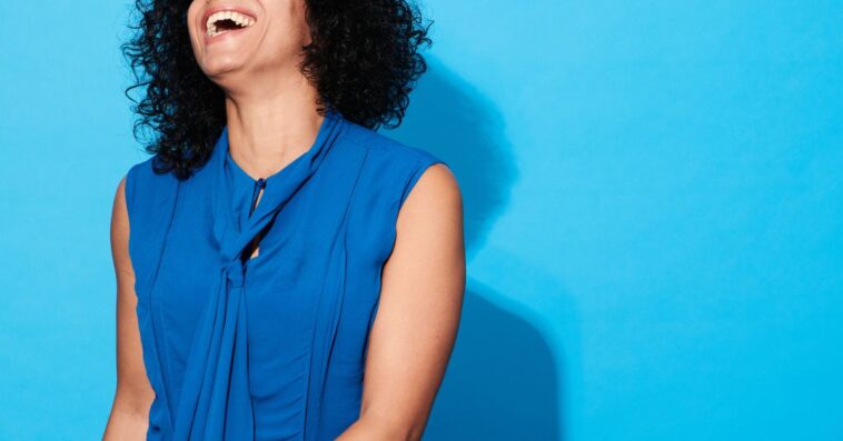 Close-up of mature woman laughing and smiling against a blue background.