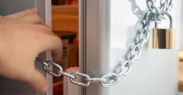 Close-up Of Person Trying To Open Fridge Locked With Chain And Padlock.
