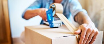 Shot of a young man sealing a box while packing up a house.