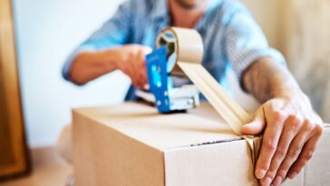 Shot of a young man sealing a box while packing up a house.