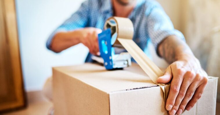 Shot of a young man sealing a box while packing up a house.