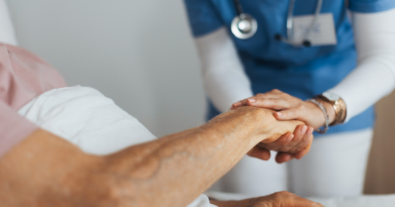 A nurse holding the hand of an older man.
