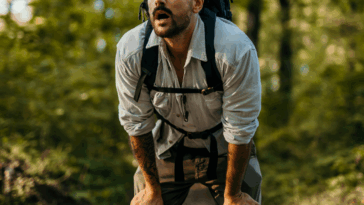 A man in hiking wear wearing a backpack bent over catching his breath.