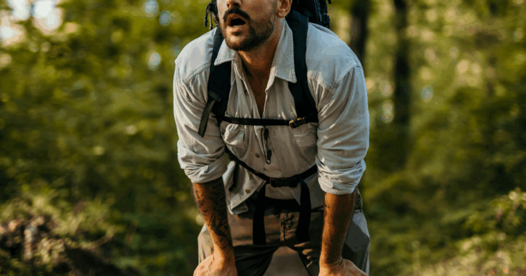 A man in hiking wear wearing a backpack bent over catching his breath.