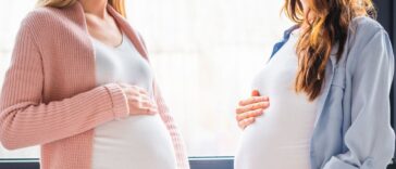 Cropped view of smiling pregnant women standing by window.