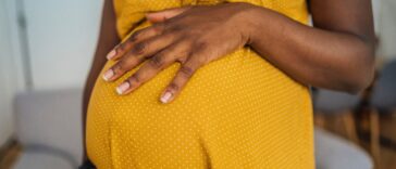 Close-up of pregnant woman in yellow dress embracing her pregnant belly.