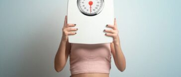 Young woman hides her face behind a bathroom scale. Studio shot.