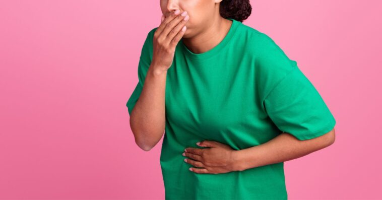 Photo portrait of a pretty young girl as she covers her mouth. She suffera nausea and wears a trendy green outfit isolated on a pink color background.